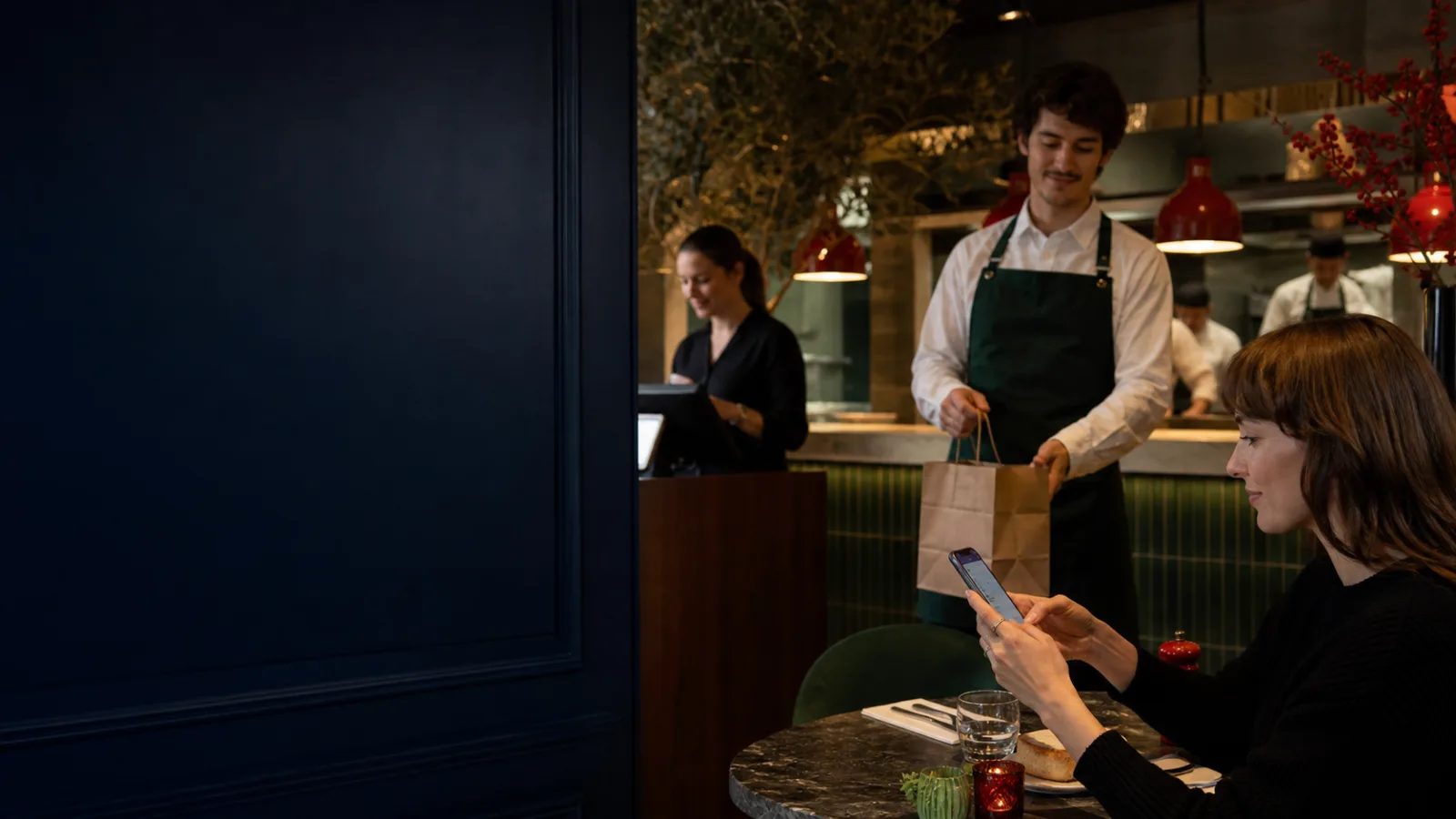 Cliente utilisant son téléphone pendant qu’un serveur prépare une commande à emporter dans un restaurant